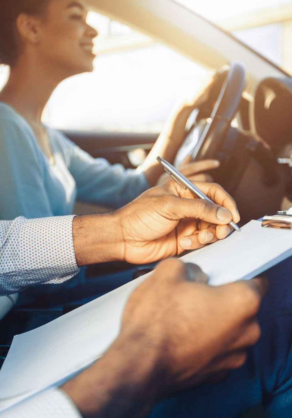 dreamstime_m_323642645 Driving Instructor Evaluating Student Woman During Lesson. A driving instructor sits in the passenger seat of a car, holding a clipboard and pen, evaluating a student who is behind the wheel. Instructor appears to be taking notes on the students performance